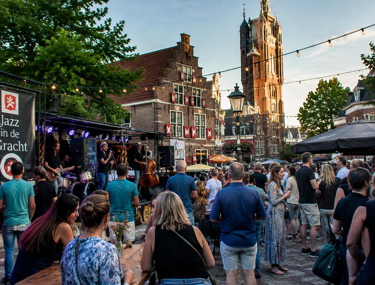 Publiek bij een openluchtconcert op een Nederlands stadsplein met lichtslingers