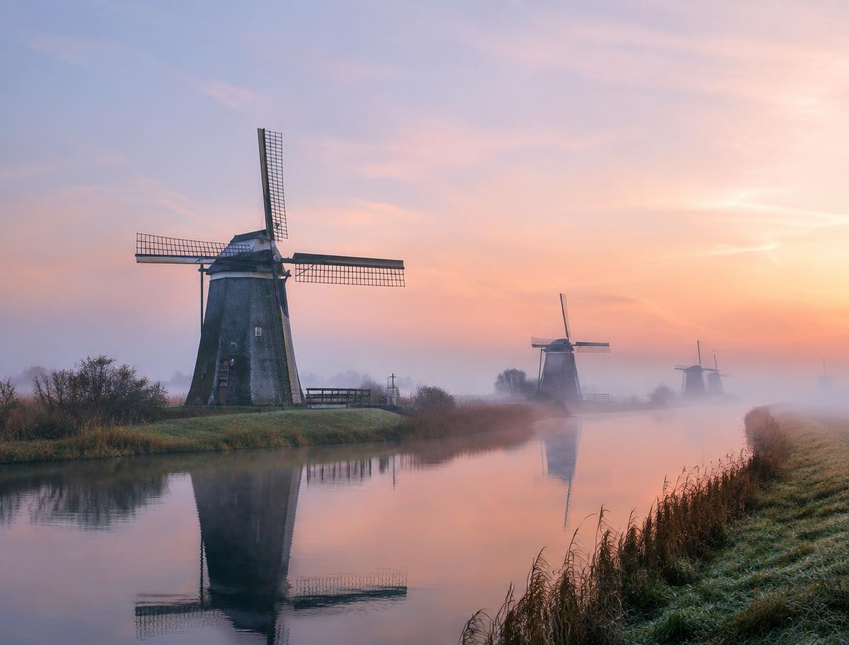 Windmolens langs een polderkanaal in de mist bij zonsopkomst